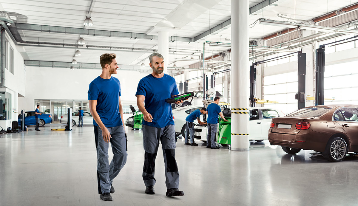 Kaksi mekaanikkoa korjaamolla. Toisella kädessään Bosch KTS -diagnostiikkalaite.