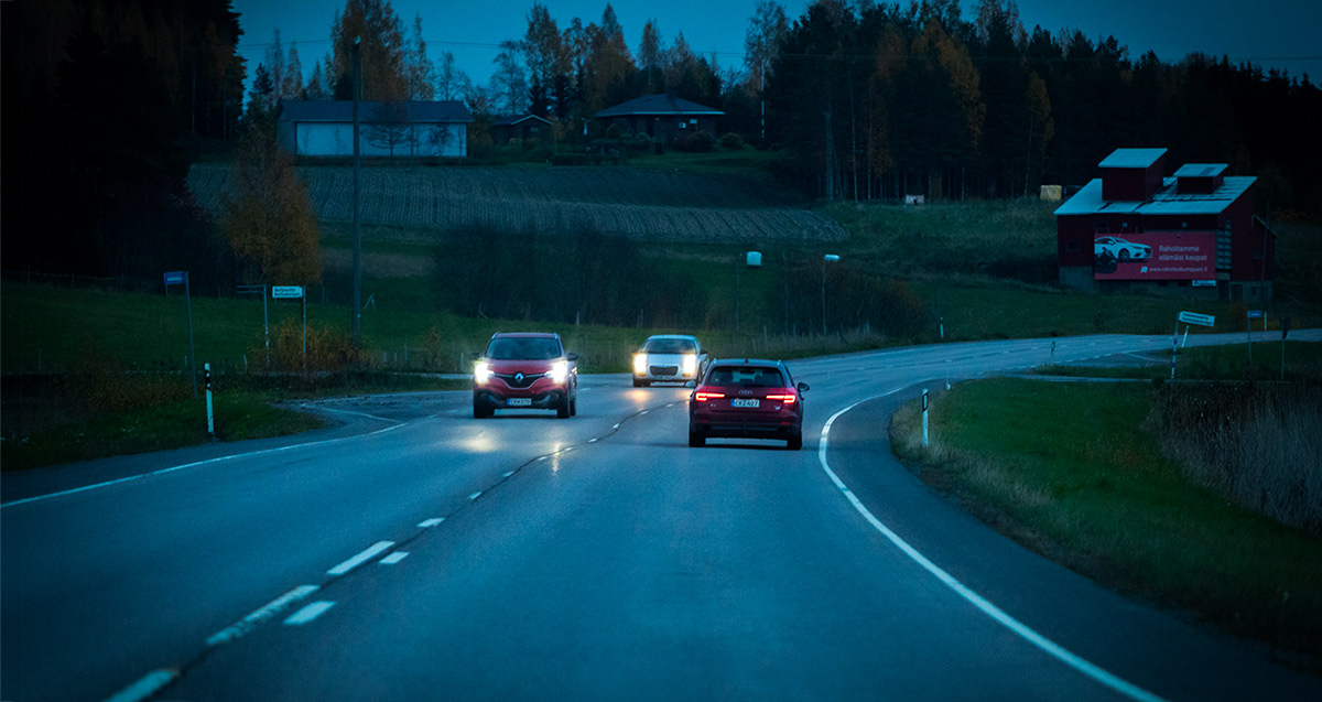 Autojen ajovalot pimeällä, syksyisellä tiellä.