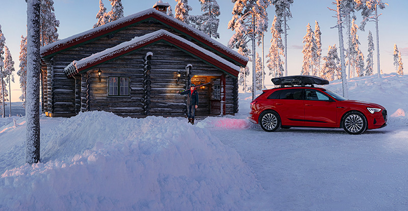 Luminen lomamökki. Laskettelija menossa autoon, jonka katolla Thule-suksiboksi.