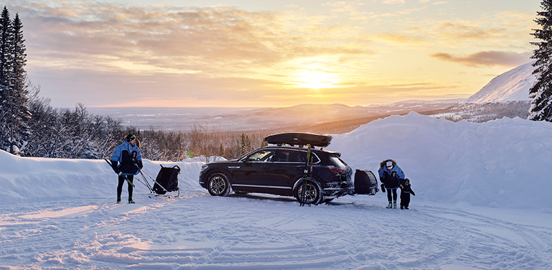 Thule-suksiboksi auton katolla ja perhe lähdössä hiihtämään.